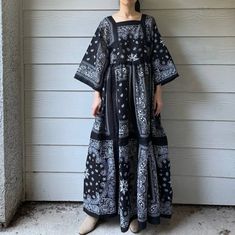 a woman standing in front of a wall wearing a black and white dress with paisley print