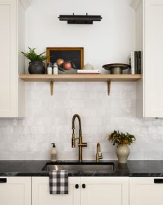 a kitchen with white cabinets and black counter tops, an open shelf above the sink