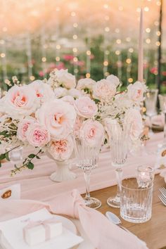 the table is set with pink and white flowers in vases, napkins, silverware, and candles