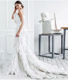 a woman in a white wedding dress standing next to a table and chair with a vase on it