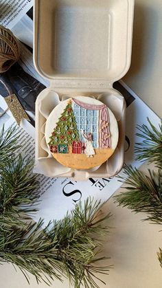 an open takeout box with a christmas scene on it and pine branches next to it