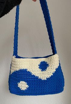 a crocheted blue and white purse hanging from a hook on the side of a wall