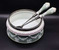 two white and green dishes with silver spoons in them on a black tablecloth