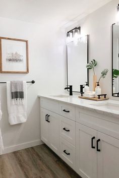 a bathroom with white cabinets and black hardware on the countertop, along with two framed mirrors