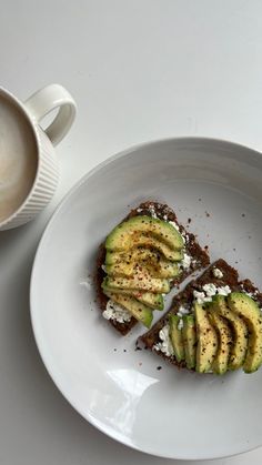 an avocado toast is on a plate next to a cup of coffee