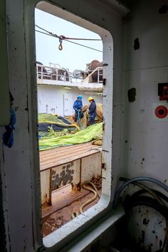 two men are working on the inside of a ship's window, while another man stands in front of it