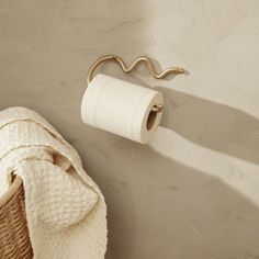 a white towel hanging on the wall next to a roll of toilet paper and a basket