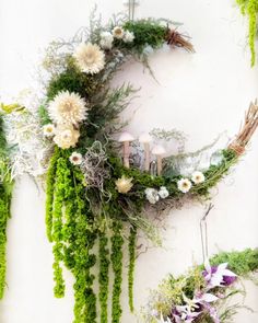 moss covered wreath with white flowers and greenery hanging on the wall next to candles