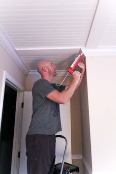 a man is painting the ceiling with a paint roller in his hand and he is holding a red tool