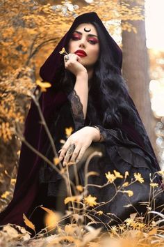 a woman with long black hair sitting in the woods