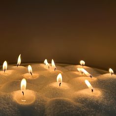 many lit candles sitting in the snow on top of each other with one candle glowing