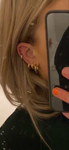 a close up of a person holding a cell phone and wearing gold earrings