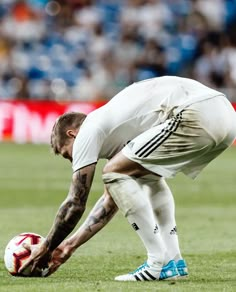 a man kneeling down on top of a soccer field holding a red and white ball