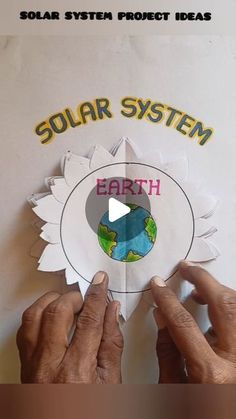 two hands holding up a paper with the words solar system on it and earth below