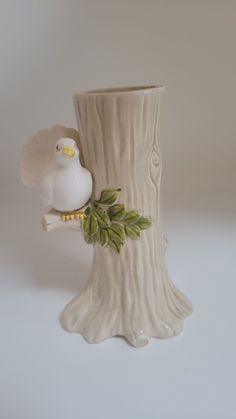 a white bird figurine sitting on top of a tree stump next to a vase