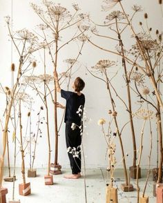 a woman is standing in front of several tall trees with white flowers on the branches