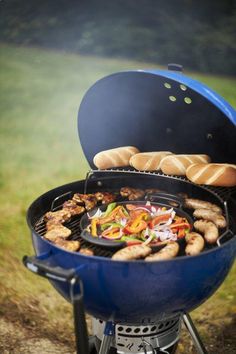 a blue bbq grill with hot dogs and vegetables cooking on it's side