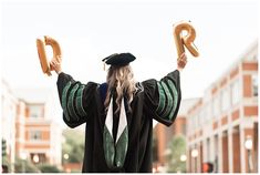 a woman in graduation gown holding two pretzels up to the sky with both hands