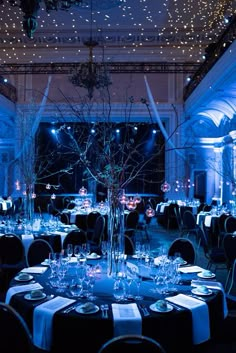 a room filled with lots of tables covered in blue lights and tall centerpieces