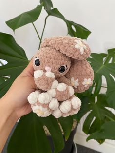 a hand holding a small stuffed animal in front of a potted plant