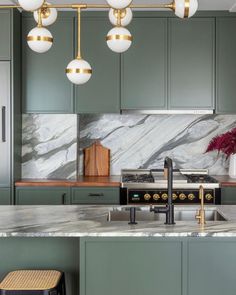 a kitchen with green cabinets and marble counter tops, gold accents on the lights over the stove