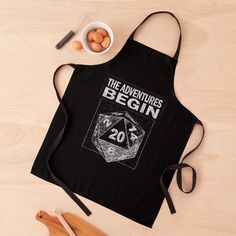 an apron that says the adventures begin with a dice on it next to eggs and utensils