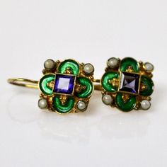 This unique Arts & Crafts Movement design showcases an onyx, iolite, blue topaz, emerald, or garnet set in a cloverleaf of emerald-green or royal blue enamel work, accented with cultured pearl. 24k gold over sterling silver. European back for pierced ears. Size: 3/4 inch. Elegant Enamel Earrings With Gemstones, Elegant Gemstone Earrings With Enamel, Vintage Enamel Jewelry With Gemstone, Vintage Enamel Gemstone Jewelry, Ornate Green Jewelry With Jewels, Antique Enamel Jewelry For Anniversary, Fine Jewelry Enamel Earrings For Formal Occasions, Elegant Enamel Jewelry With Gemstone, Formal Enamel Earrings In Fine Jewelry Style