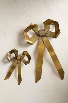 two pieces of art made out of metal on a white wall and one piece is shaped like an origami