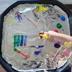 a child is playing with plastic spoons and toothbrushes on an aluminum foil covered tray