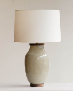 a white table lamp with a beige shade on it's base and a brown wooden base