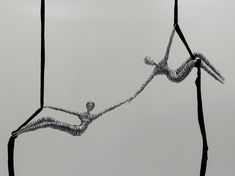 two wire sculptures hanging from wires in front of a gray sky with no one on it