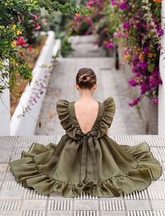 a woman is sitting on the ground in a green dress and looking at some flowers