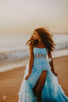 a woman in a blue dress standing on the beach with her hair blowing in the wind