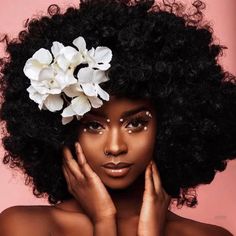 a woman with an afro and flowers in her hair is posing for the camera on a pink background