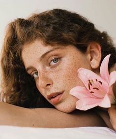 a woman with freckled skin holding a pink flower