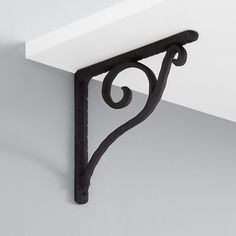 the corner of a shelf with a decorative iron bracket on it's side, against a white wall