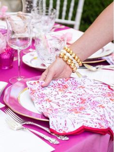 a person setting a table with place settings and napkins on it, along with wine glasses