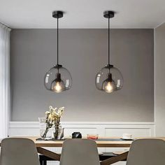 three lights hanging over a dining room table with chairs and vases on the table