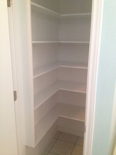 an empty closet with white shelving and tile flooring in the corner between two doors