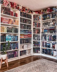 a room filled with lots of books on top of white shelving units next to a rug