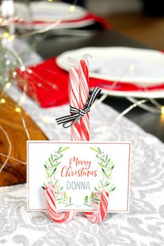 a candy cane with a merry christmas sign on it sitting on a table next to plates and napkins