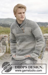 a young man sitting on top of a stone wall wearing a gray sweater and jeans