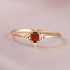 a yellow gold ring with an oval shaped red stone surrounded by small white diamond accents