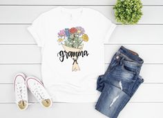 A perfect, personalized tee for any mom, grandmother, or auntie - this graphic tee features your choice of birth month flower for a totally personalized and custom gift! Choose your month(s) and I'll bring to life a custom birth flower bouquet complete with the name of the recipient front and center. This is a one of a kind, unique gift that would make any Mother's Day surprise complete! Product Details: This short sleeve tee is professionally printed from my original drawing! Bella short sleeve Custom Print Cotton T-shirt For Personalized Gift, Custom Print T-shirt As Personalized Gift, Personalized White Top For Spring, Personalized Short Sleeve T-shirt For Spring, Personalized Mother's Day T-shirt With Custom Text, Personalized T-shirt For Spring Gift, Custom Text T-shirt For Mother's Day Personalized Gift, Custom Text T-shirt For Mother's Day Gift, Personalized Casual Spring T-shirt