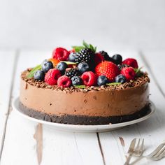 a chocolate cake topped with berries and mint leaves on top of a white wooden table