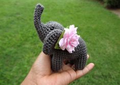 a small crocheted elephant holding a pink flower in its trunk, with grass behind it