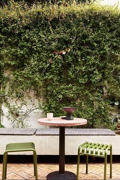 two green chairs sitting at a table in front of a wall covered with greenery