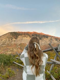 a woman with long hair standing in front of mountains