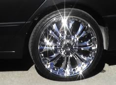 the front wheel of a black car with chrome spokes and bright lights on it