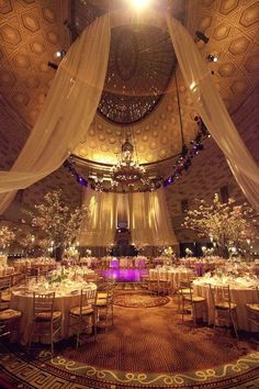 a banquet hall with tables and chairs covered in white drapes, decorated with floral centerpieces